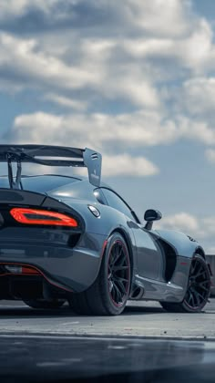 a grey sports car parked on top of a parking lot with cloudy skies in the background