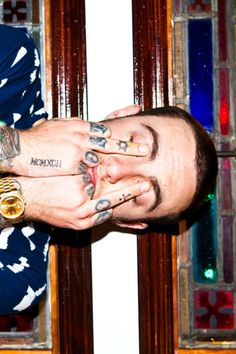 a man with tattoos and piercings on his fingers standing in front of stained glass windows