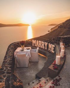 an outdoor seating area with candles and flowers on the ground next to water at sunset