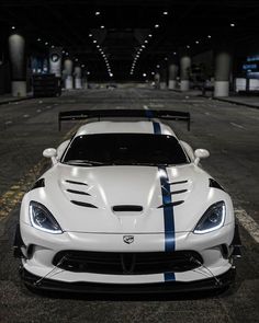 a white sports car with blue stripes parked in a parking lot at night, front view