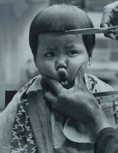 a young child is being brushed by an older person with scissors on their head and his tongue sticking out