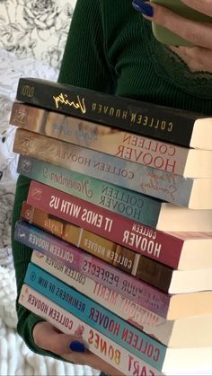 a stack of books sitting on top of a bed next to a woman's hand