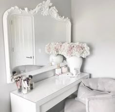 a white vanity with flowers in a vase on it and a chair next to it