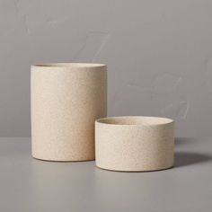 two white vases sitting next to each other on a gray surface with a wall in the background