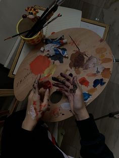 a woman is painting with her hands on an easel in front of some paintbrushes