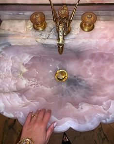 a woman's hand is touching the edge of a pink sink with gold faucets