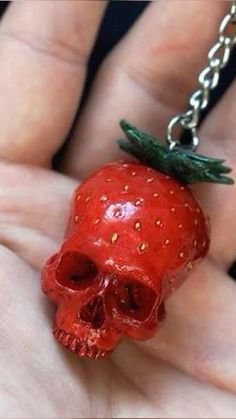 a hand holding a red strawberry with a skull head on it's side and a silver chain