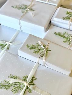 several wrapped presents with white bows and green leaves on them, all tied up together