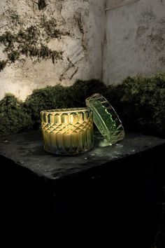 two yellow candles sitting on top of a table next to moss covered walls and a wall