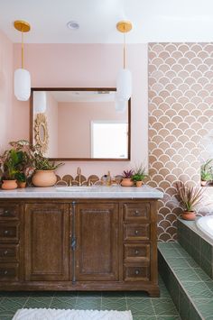 a bathroom with pink walls and green tile flooring, along with a wooden vanity topped with potted plants