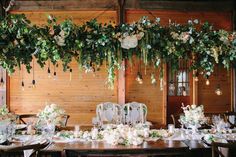 the table is set with white flowers and greenery hanging from the ceiling over it