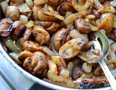 a pan filled with onions and mushrooms on top of a stove next to a spoon