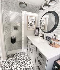 a white tiled bathroom with black and white tile on the floor, mirror above the sink