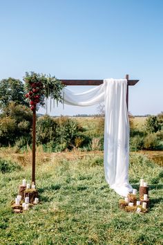 an outdoor ceremony setup with white drapes and greenery on the grass, surrounded by candles