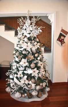 a white christmas tree with silver ornaments and bows on it in the corner of a room