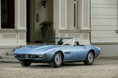 an old blue sports car parked in front of a large building with columns and pillars