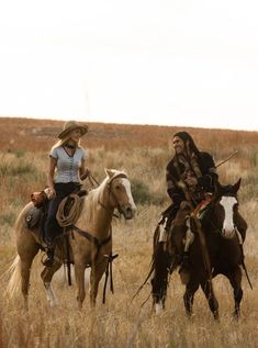 two women riding horses in the middle of a field with tall grass and dry grasses