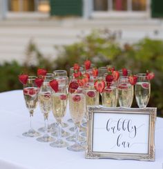 there are many wine glasses with strawberries in them and a sign on the table