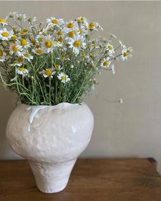 a white vase filled with daisies on top of a wooden table