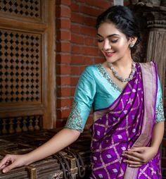 a woman in a purple and blue sari is standing next to an old trunk