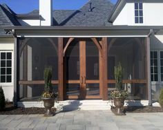 the front entrance to a house with potted plants on either side and large wooden doors