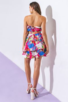 a woman standing in front of a white wall wearing a colorful dress and high heels