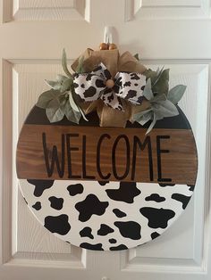 a cow print welcome sign hangs on the front door with burlocks and greenery