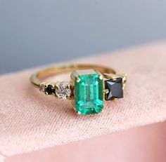 an emerald and black diamond ring sitting on top of a pink cloth covered tablecloth