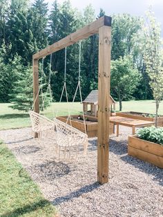 a wooden swing set in the middle of a graveled area next to some trees