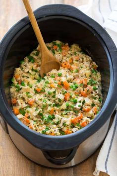 a wooden spoon in a slow cooker filled with rice and vegetables