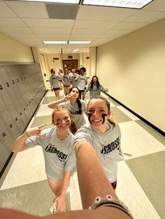 two girls are pointing at the camera in a hallway with lockers on both sides