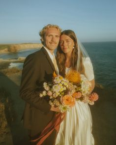 a bride and groom standing next to each other in front of the ocean