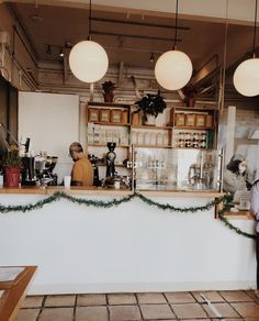 two people standing in front of a counter with lights hanging from it's ceiling