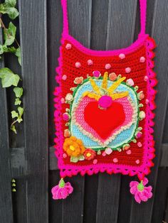 a crocheted bag hanging on the side of a fence with flowers and hearts