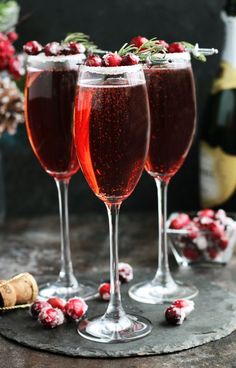 three glasses filled with wine and garnished with cranberries on a table