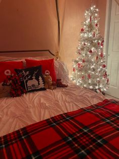 a christmas tree in the corner of a bedroom with red and white plaid bedding