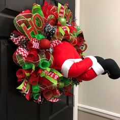 a christmas wreath with santa claus's hat hanging from the front door, decorated with green and red ribbons