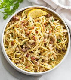 a white bowl filled with pasta and meat on top of a marble table next to a lemon wedge