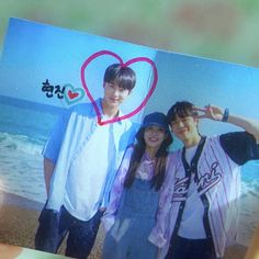 two people are holding up a photo with a heart on the beach in front of them