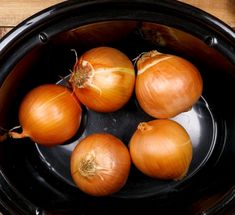 four onions are sitting in the bottom of a slow cooker, ready to be cooked