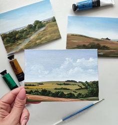 someone is holding up some paintings on the table