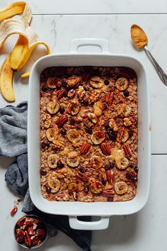 a white casserole dish filled with granola and nuts next to two bananas