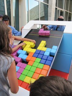 a group of people standing around a table with colorful blocks on it and two children playing