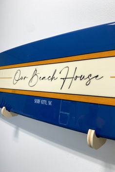 a blue surfboard with the words our beach house on it hanging from a wall