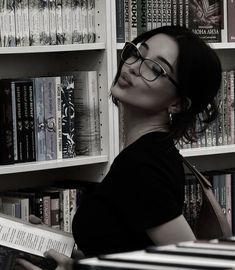 a woman in glasses is leaning against a book shelf and looking up at the books