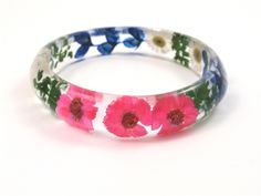 "This lightweight Slip on Bangle is made with Real Dried bright pink and white daisies, Texas bluebonnet and green leaves embedded into crystal clear resin and shaped into a unique and stylish bangle with Glassy finish that sparkles in the light. It is a chunky bangle with a curved profile; thicker in the center and tapering on the sides. This stunning bangle embodies contemporary resin jewelry for the nature lover. Bracelet measures: Inside diameter 2 3/4\" (69mm) high 5/8\" (16mm ) thick 11/64 Adjustable Flower Bracelets With Pressed Flowers, Multicolor Flower Jewelry With Pressed Flowers, Multicolor Flower Shaped Jewelry With Pressed Flowers, Adjustable Pink Jewelry With Pressed Flowers, Adjustable Bracelets With Pressed Flowers, Adjustable Round Bracelets With Pressed Flowers, Lover Bracelet, Flowers Daisy, Texas Bluebonnets