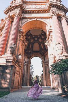 a woman in a purple dress is walking under an archway