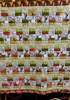 a quilted blanket with pictures of birds and grass in the foreground, on top of a wooden table