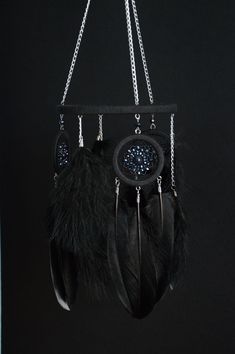 a black and white dream catcher with feathers hanging from it's side on a chain