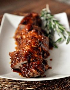 a white plate topped with meat covered in bbq sauce and garnished with herbs